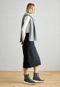 Bufanda de lana gris drapeada sobre una camisa blanca de manga larga, combinada con una falda negra de longitud media y zapatillas gris de caña baja con suelas blancas.