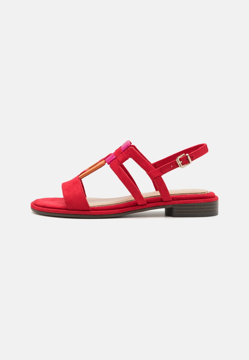Sandale en daim rouge avec un talon plat, présentant une pointe ouverte et un design découpé. Sangle de cheville ajustable avec une boucle en argent et des accents colorés.