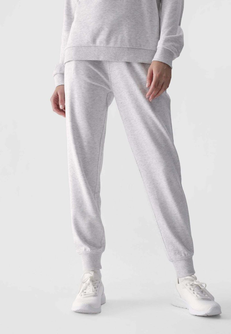 Helle graue Jogginghosen aus weichem Stoff, mit einem elastischen Bund und Bündchen, kombiniert mit weißen Sportschuhen.