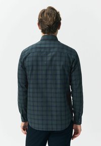 Camicia a maniche lunghe in cotone verde scuro con un motivo a scacchi blu navy e verde chiaro. Presenta un colletto con bottoni e un orlo arrotondato.