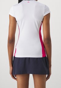 Top atlético blanco con mangas cortas, que presenta un panel lateral rosa. Combinado con una falda plisada de color azul marino oscuro, hecha de tela transpirable.