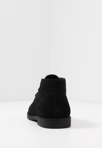 Bottines en suede noir avec une texture lisse, bout rond et semelle en caoutchouc plate et basse. Présente un design à lacets et des détails de couture minimalistes.