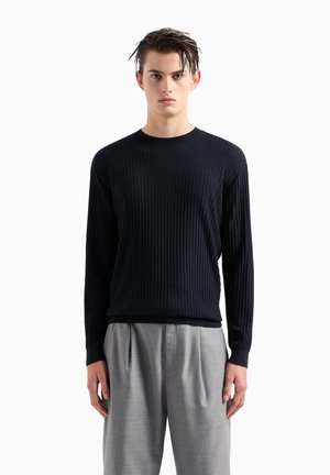 Maglione a coste blu navy con scollo rotondo, maniche lunghe e silhouette aderente, abbinato a pantaloni beige chiaro sartoriali.