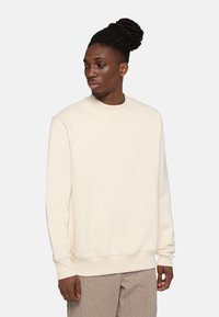 Sudadera de color beige claro con escote redondo. Tejido suave, puños y dobladillo acanalados. Presenta un pequeño y sutil logo en el pecho.