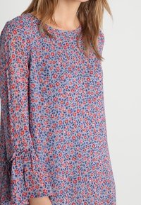 Robe à motif floral en tissu doux, présentant une base bleue avec des accents rouges et violets, un col rond et des manches à volants.