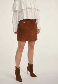 Brąspiana zamszowa mini spódniczka z dwiema przednimi kieszeniami, złotymi guzikami i miękką fakturą, w połączeniu z brązowymi zamszowymi botkami za kostkę.