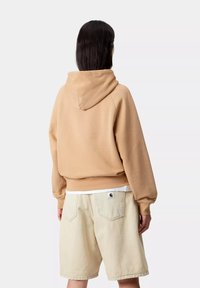 Sudadera beige con capucha ajustable y dobladillo acanalado, combinada con pantalones cortos de mezclilla beige claro con bolsillos traseros.