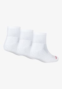 Tres pares de calcetines de tobillo de algodón blanco con parte superior acanalada, con un acento de logo rojo en la suela. Textura suave y diseño de color sólido.