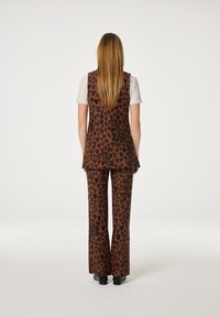 Bruin vest en broekset met een zwart hartpatroon. Het vest is iets langer en gecombineerd met uitlopende broeken, beide gemaakt van glad materiaal.