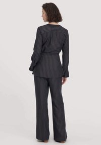 Completo nero a righe verticali con giacca aderente e pantaloni a zampa. Tessuto morbido, righe verticali colorate e maniche lunghe con polsini.