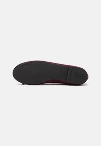 Ballerines en suède bordeaux avec une semelle en caoutchouc noir lisse. Présente un logo embossé sur la semelle et un design à bout arrondi.
