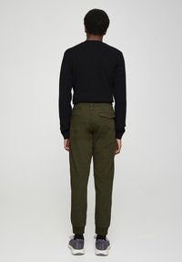 Olijfgroene, taps toelopende cargobroek met omgeslagen zoom, zijzakken en een achterzak. Draagt ze met een zwart shirt met lange mouwen en grijze sneakers.