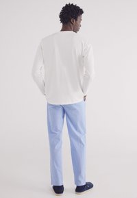 Camicia bianca a maniche lunghe abbinata a pantaloni a righe blu e bianche. I pantaloni hanno una vestibilità dritta e la camicia presenta un collo rotondo.