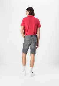 Polo rose, shorts en denim gris, baskets blanches et chaussettes mi-mollet. Les shorts ont une texture délavée avec un accent noir à la taille.