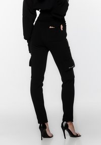 Czarne spodnie cargo wykonane z miękkiego materiału, charakteryzujące się dopasowanym krojem, bocznymi kieszeniami i akcentem z logo marki. W połączeniu z czarnymi sandałami na wysokim obcasie.