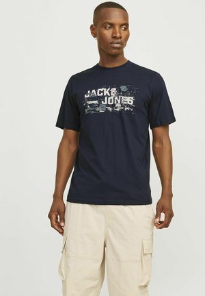 Marineblå bomulds T-shirt med et falmet "JACK & JONES" print i hvid og grå. Korte ærmer, rund hals, afslappet pasform.