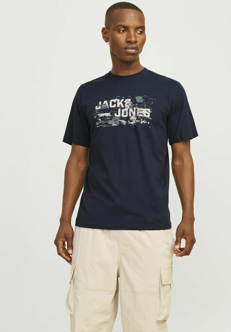 Zilas kokvilnas T-krekls ar izbalējušu "JACK & JONES" printu baltā un pelēkā krāsā. Īsas piedurknes, apaļa izgriezuma kakla daļa, brīvs griezums.