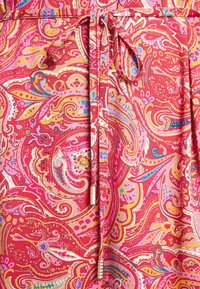 Punainen paisley-kangas, jossa on vaaleanpunaisia, keltaisia ja sinisiä yksityiskohtia. Mukana on solmittava vyö, jossa on tekstuuritietoja. Pehmeä, kuvioitu pinta läpi koko kankaan.