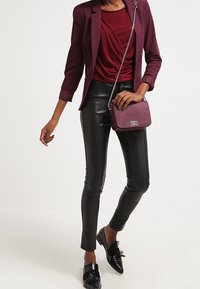 Burgunder blazer over en draperet burgunder top, parret med skinnende sorte faux læderbukser og sorte loafers med sløjfe-detaljer. Crossbody-taske medfølger.