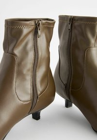 Bottes chelsea en cuir verni marron avec une fermeture éclair sur le côté, bout arrondi et petit talon. Texture lisse avec des coutures décoratives.