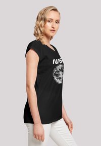 Schwarzes Baumwoll-T-Shirt mit einem NASA-Logo und einer Erd-Grafik auf der Vorderseite, Kapärmel und einer lockeren Passform. Der Text ist weiß.