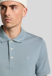 Hemelsblauwe polo met een gestructureerde stof, voorzien van een drieknopenlijst, geborduurd logo op de borst en een klassieke kraag.