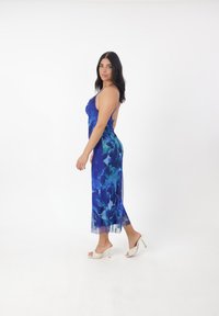 Blå blomstrete slipdress med tynde stropper, gennemsigtigt stof og en længde til midt på læggen. Sammen med lyse hæle.