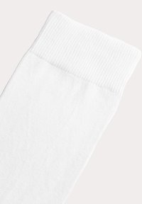 Hvid sok med en ribbet kant, lavet af blød stof. Har en ren, glat tekstur og en afsmalnet form langs foden.