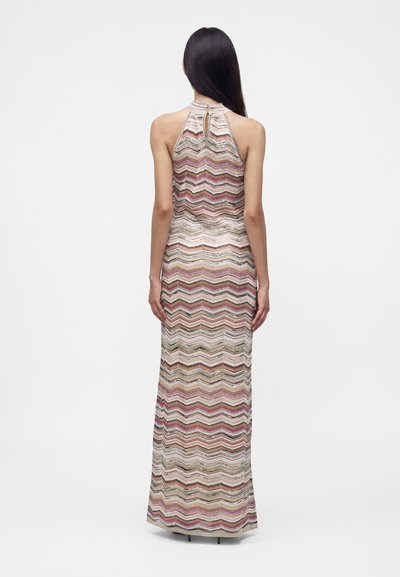 Femme aux longs cheveux foncés portant une robe longue sans manches avec un motif zigzag multicolore, vue de dos.