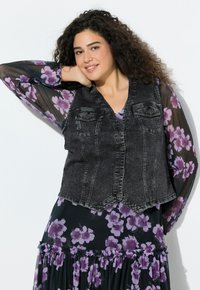 Czarna denimowa kamizelka z dekoltem w serek, przednimi kieszeniami i zapięciem na guziki. Pod spodem sukienka w kwiatowy wzór z fioletowymi akcentami i falbankami.