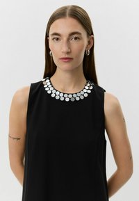 Zwart mouwloos jurkje met een ronde halslijn versierd met ronde zilveren paillettes, gladde stof en een relaxte pasvorm.