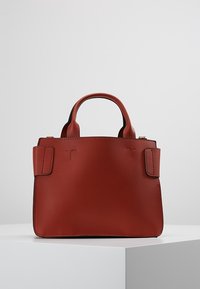 Petit sac à main en cuir rouge avec deux poignées courtes, de forme rectangulaire, détails en relief à l'avant et design minimaliste.