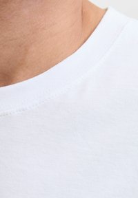 Bijeli pamučni t-shirt ovratnik s glatkom teksturom, s čistim šavom i izrezom, otkriva kožu uz tkaninu.