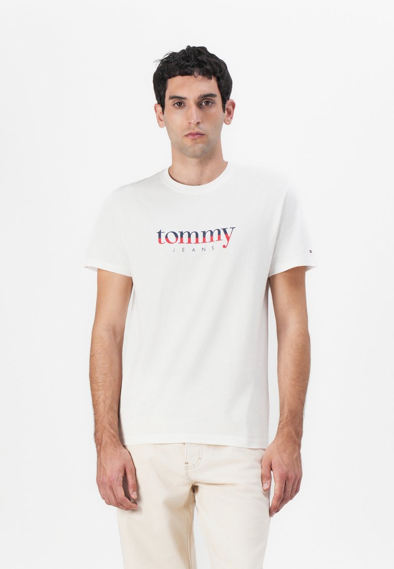 Hvit bomull T-skjorte med rund hals, med en blå og rød "tommy" logo over "JEANS" i matchende farger. Korte ermer, simpelt design.