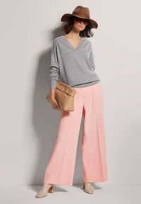 Grijze v-hals trui, brede perzikkleurige broek, beige tas en lichtbruine blokhak-schoenen. Geassocieerd met een bruine hoed en zonnebril.