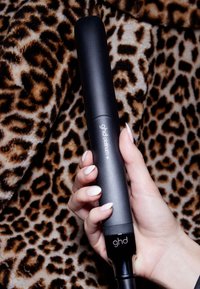 Hand die een zwarte ghd platinum+ haarstijltool vasthoudt tegen een achtergrond van luipaardprint stof.