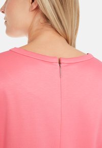 Roze top met een gladde textuur, voorzien van een ronde halslijn en een korte, discrete rits aan de achterkant. Eenvoudig, strak ontwerp.