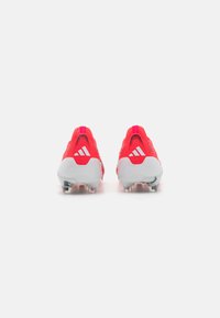 Red athletic cleats with a textured upper, white accents, and a molded sole. Features angular heel design and visible studs for traction.
