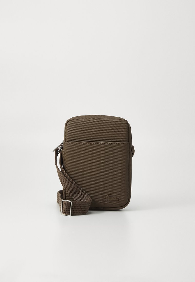 Sac bandoulière texturé marron en matériau durable, de forme rectangulaire, avec fermeture zippée et une bandoulière réglable. Logo Lacoste visible.