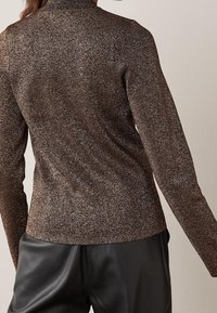 Maglietta a maniche lunghe in tessuto metallico marrone con un design aderente, caratterizzata da un collo alto e una textura liscia, abbinata a pantaloni in pelle nera.