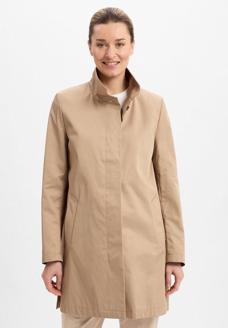 Beige trenchcoat met een staande kraag, voorzakken en een strakke silhouet. Gemaakt van lichtgewicht materiaal met een soepele textuur.