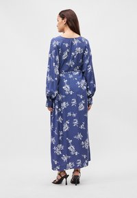 Maxi φόρεμα από navy ύφασμα με λευκή floral εκτύπωση. Μακριά μανίκια, ελαστική μέση και ρέουσα σιλουέτα. Φοριέται με μαύρες ψηλές γόβες.