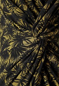 Tissu noir avec un motif de feuilles de palmier en vert foncé et or, présentant une texture torsadée qui crée des plis drapés.