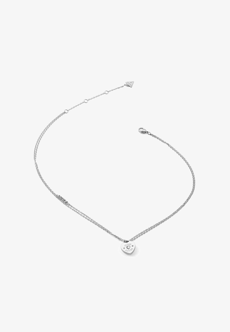Collier en argent avec un design à double chaîne. Pendentif en forme de cœur avec des gravures et des accents décoratifs. Texture lisse, style minimaliste.