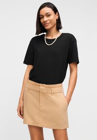 T-shirt noir à manches courtes associé à une mini-jupe beige à fines rayures, avec une ceinture élastique et des poches avant.