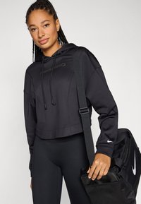 Black cropped hoodie with drawstrings and "Nike Pro" logo, paired with black leggings. Holding a black bag with a white Nike swoosh.
