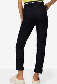Pantaloni in denim blu scuro con vita aderente, gamba dritta e dettagli sulle tasche posteriori. Accentuati da una cintura con righe bianche.
