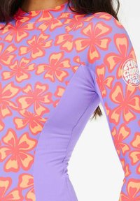Rash guard de manga larga que presenta una vibrante tela morada con grandes patrones florales en naranja y rosa, y textura acanalada en las mangas.