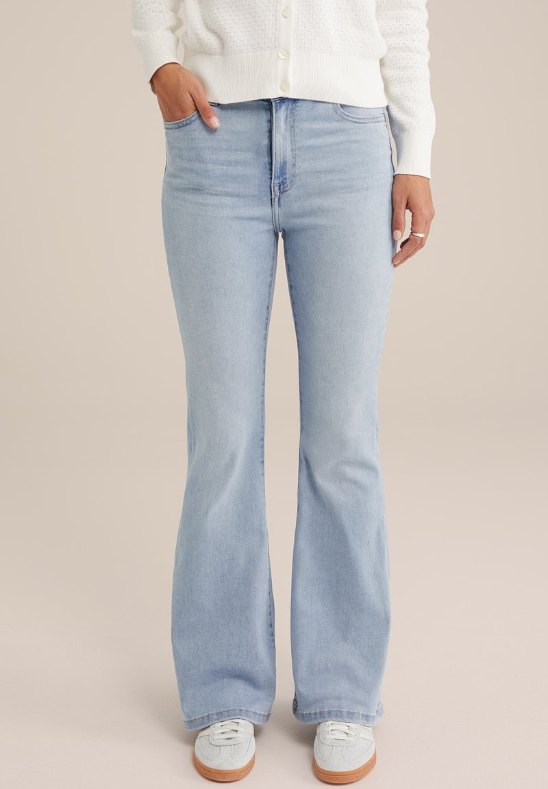 Svijetloplave traperice šišrnog kroja, s visokim strukom i prednjim džepovima. Uparene sa svijetlim tenisicama, postavljene na neutralnoj pozadini.