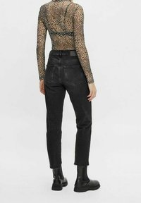Jeans denim hitam dengan pinggang tinggi, kaki menyempit, dan hem yang frayed. Dipadukan dengan atasan lengan panjang transparan bercorak leopard dan sepatu bot hitam.